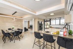 A modern kitchen with a large island, black bar stools, and a dining area with a table and chairs. - Luxury 5BR Huge Oasis by the Shuk (Jerusalem)