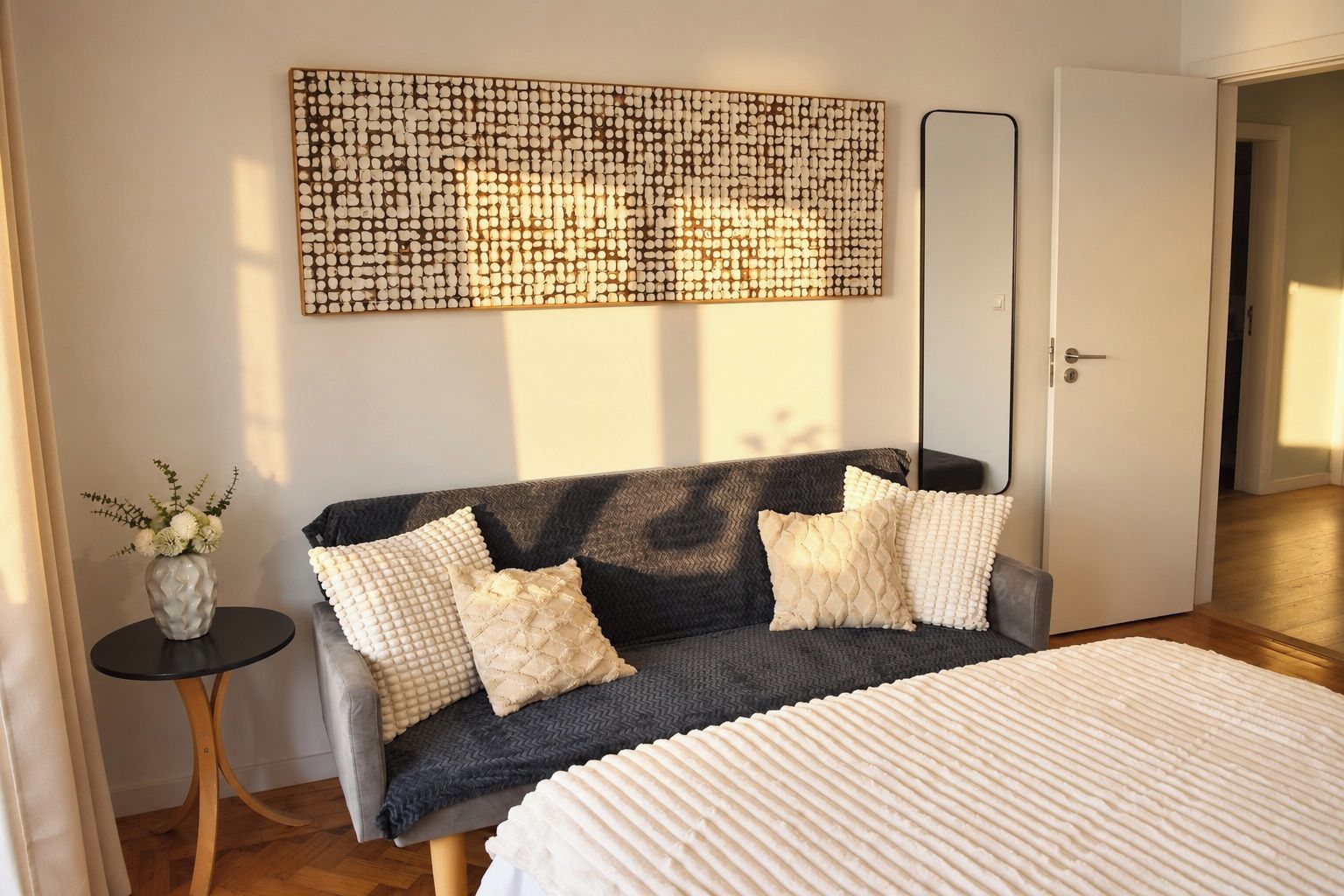 Ett sovrum med en säng, en soffa, ett konstverk på väggen, ett litet bord med en vas och en dörr.