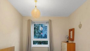 A bedroom with a bed, a window with curtains, a wooden dresser, and a hanging light fixture.