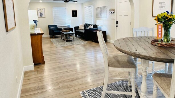 A spacious living room with a wooden floor, a round dining table, and a kitchen area visible through an archway. - Clean, Cute, and Comfortable (Safford)