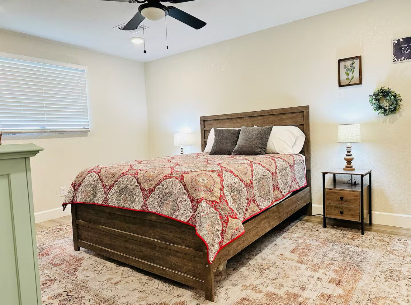 Une chambre à coucher avec un lit en bois, une couvre-lit à motifs, des tables de chevet et un ventilateur de plafond.