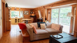 L’intérieur chaleureux d’un chalet avec un canapé à rayures, un fauteuil rouge, une table à manger en bois et une grande fenêtre donnant sur le paysage extérieur.