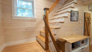 Un escalier en bois avec une rampe, une fenêtre et un four à micro-ondes posé sur un meuble.