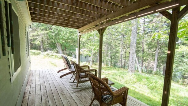 Une terrasse en bois, dotée de chaises en osier, qui offre une vue sur une forêt.