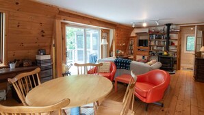 L’intérieur chaleureux d’un chalet avec une table à manger en bois, des chaises, un canapé rouge, une bibliothèque et une cheminée.