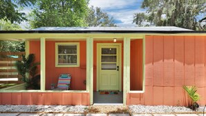 A small, single-story house with a bright orange exterior, a green door, and a small porch area with a striped chair and a small table. - The Tropical Palms ~ Cowboy Pool ~ Private yard. (St. Augustine)