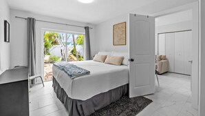 A bedroom with a bed, a desk, a chair, a door, and a view of the outdoors.