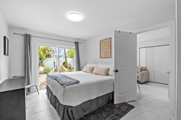 A bedroom with a bed, a desk, a chair, a door, and a view of the outdoors. - Guava getaway freshly renovated unit September 2025 heated pools (Clearwater)