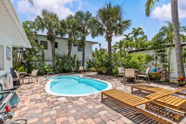 A pool area with lounge chairs, palm trees, and a brick patio. - Guava getaway freshly renovated unit September 2025 heated pools (Clearwater)