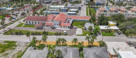 A coastal resort area with a large building featuring red-tiled roofs, a swimming pool, and a beach in the background.
