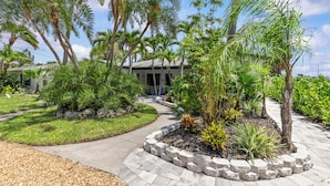 A landscaped garden with palm trees, a curved pathway, and a building with a gray roof.