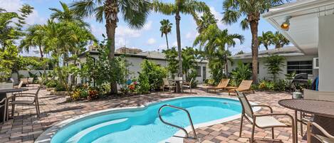 Une piscine d’une profondeur de 1 mètre 10, entourée de palmiers et agrémentée de mobilier d’extérieur.