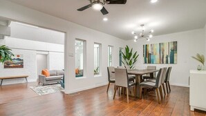 A modern dining area with a wooden table and chairs, a ceiling fan, and a white brick wall with a painting. - Spacious 6-bedroom house in delightful Grand Prairie with Pool (Grand Prairie)