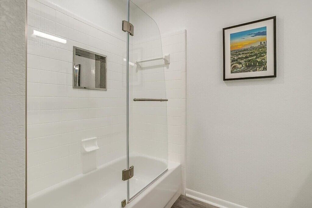 A bathroom with white tiled walls, a glass shower enclosure, a bathtub, and a framed picture on the wall.
