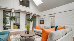 A modern living room with a grey sofa, orange cushions, a round coffee table, and potted plants. - Spacious 6-bedroom house in delightful Grand Prairie with Pool (Grand Prairie)
