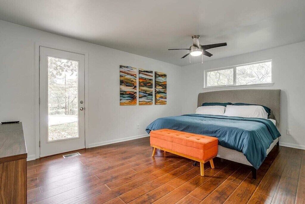 A bedroom with a bed, a ceiling fan, a window, and artwork on the wall.