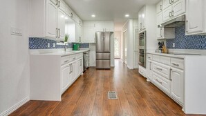 A modern kitchen with white cabinetry, a stainless steel refrigerator, and a blue-tiled backsplash. - Spacious 6-bedroom house in delightful Grand Prairie with Pool (Grand Prairie)