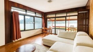 A spacious living area with a large sofa, a small round table, and a view of a lake through large windows.