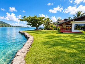 A beachfront property with a stone wall, a well-maintained lawn, and a modern house with a red roof.