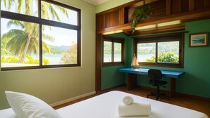 A room with a bed, a desk, and a view of palm trees and mountains. - Faratea Bayhouse - Seaside, large garden, unique panoramic view. (Moorea)