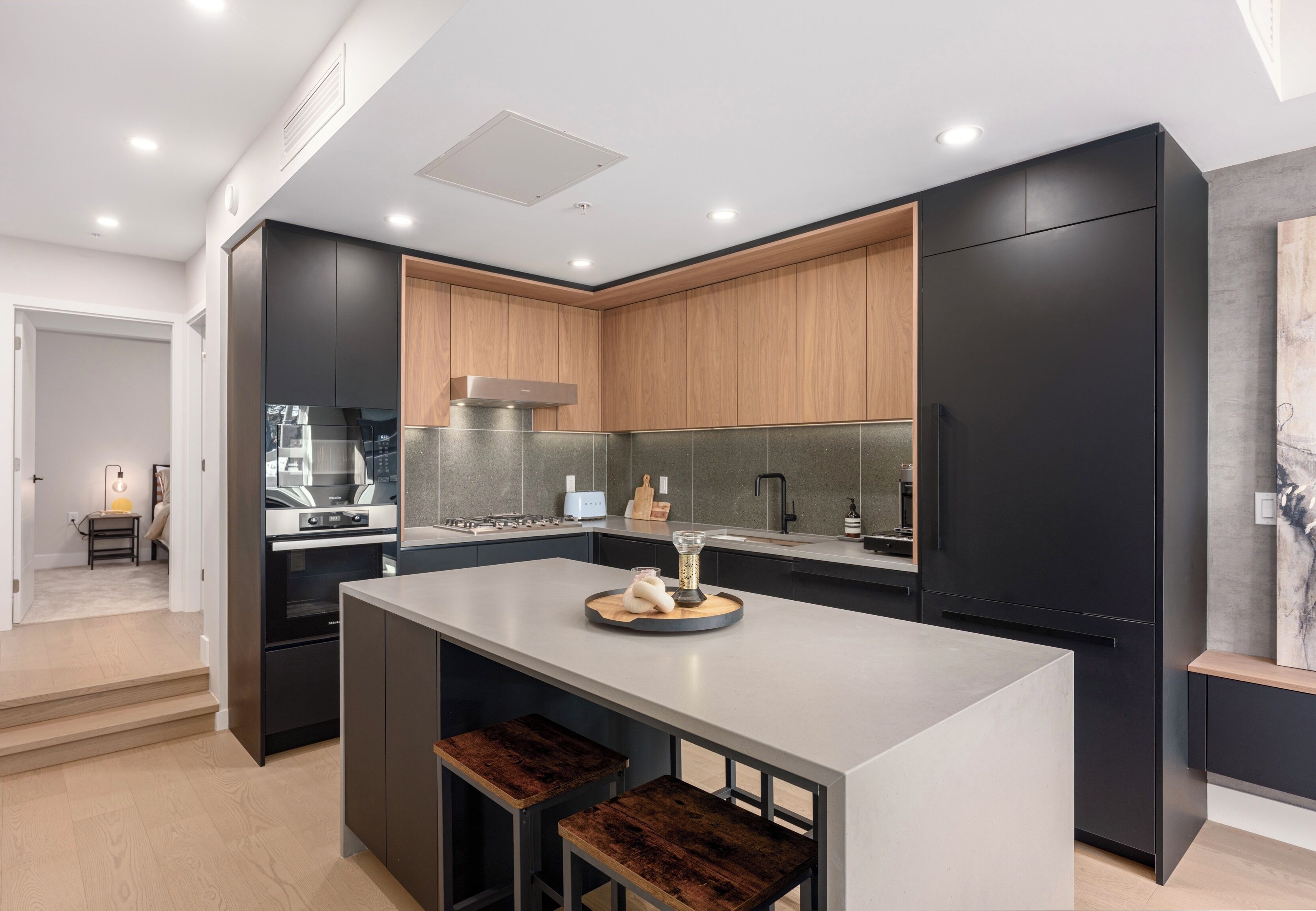 A modern kitchen with a central island, dark cabinetry, and a wooden accent wall.