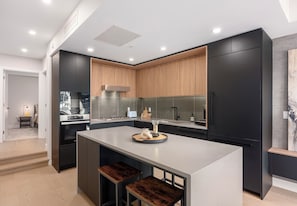 A modern kitchen with a central island, dark cabinetry, and a wooden accent wall.