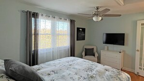 Een slaapkamer met een bed, een plafondventilator, een dressoir, een stoel en een televisie aan de muur.