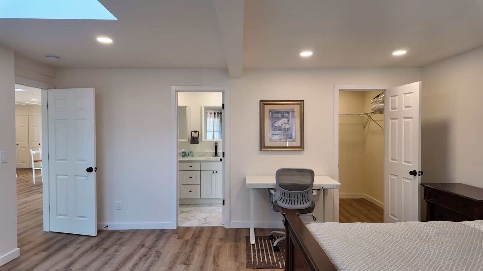 A bedroom with a bed, a desk, and a chair. There is a door leading to a bathroom.