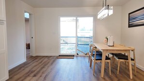 Una habitación amplia con piso de madera, un ventanal corredero que da a un balcón, una mesa de comedor con sillas y un cuadro en la pared.