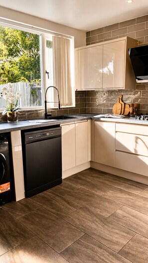 A modern kitchen with a dishwasher, a sink, and a window with curtains.