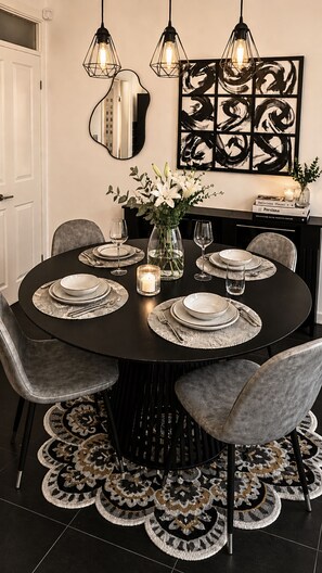 A dining area with a round table set for four, surrounded by chairs, with a mirror and artwork on the wall.
