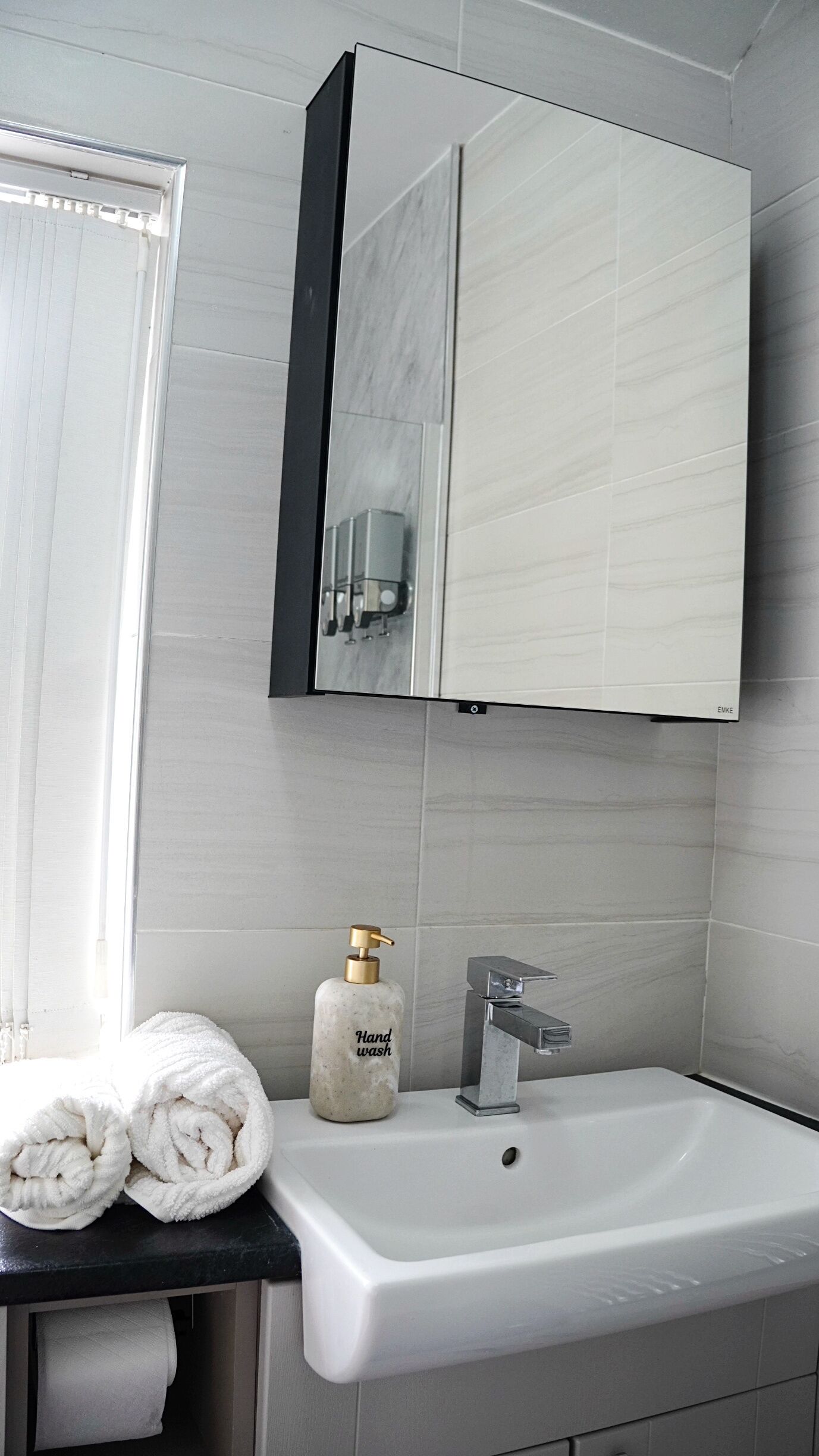 A bathroom with a white sink, a mirror, and a hand wash dispenser.