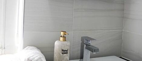 A bathroom with a white sink, a mirror, and a hand wash dispenser.