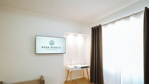 Una sala de estar moderna con un sofá, un escritorio y un televisor que muestra “RENA BIANCA APARTMENTS”.