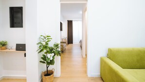 Una sala de estar moderna con un sofá verde, piso de madera, una computadora portátil sobre una estantería y una planta en maceta.