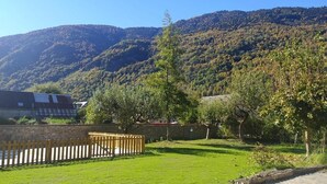 Un área con césped, una valla de madera, árboles y un edificio al fondo.