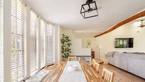 Ein geräumiger Wohnbereich mit einem langen Holzespeisetisch, einem grauen Sofa und einem großen Fenster mit Jalousien.