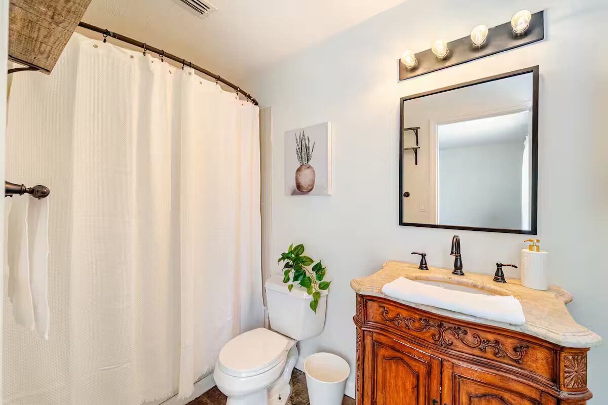 A bathroom with a white toilet, a wooden vanity with a mirror, and a shower curtain.