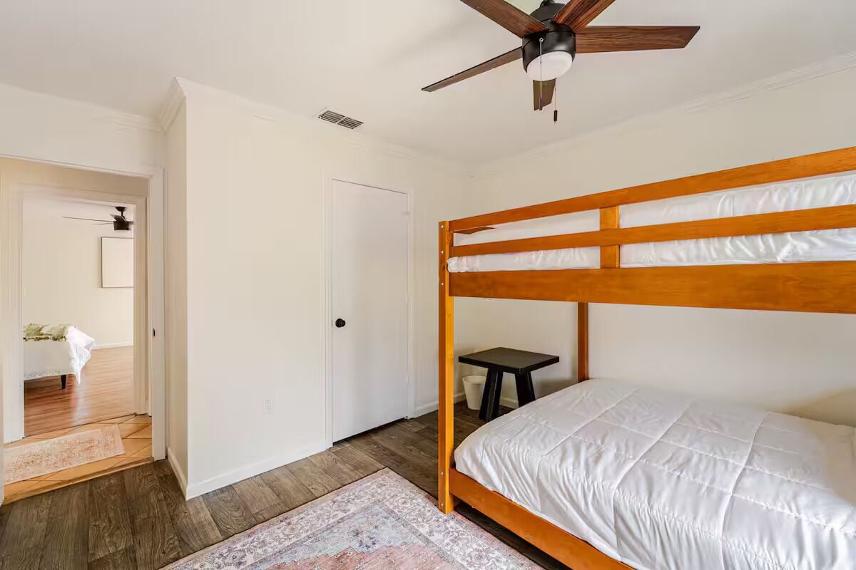 Un dormitorio con una cama litera de madera, un ventilador de techo, una mesita pequeña y una alfombra.