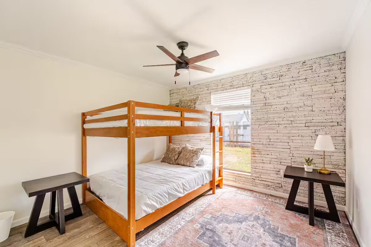 A bunk bed room with a brick wall, a ceiling fan, and a window with blinds.