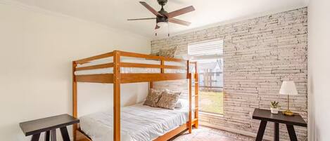 A bunk bed room with a brick wall, a ceiling fan, and a window with blinds.