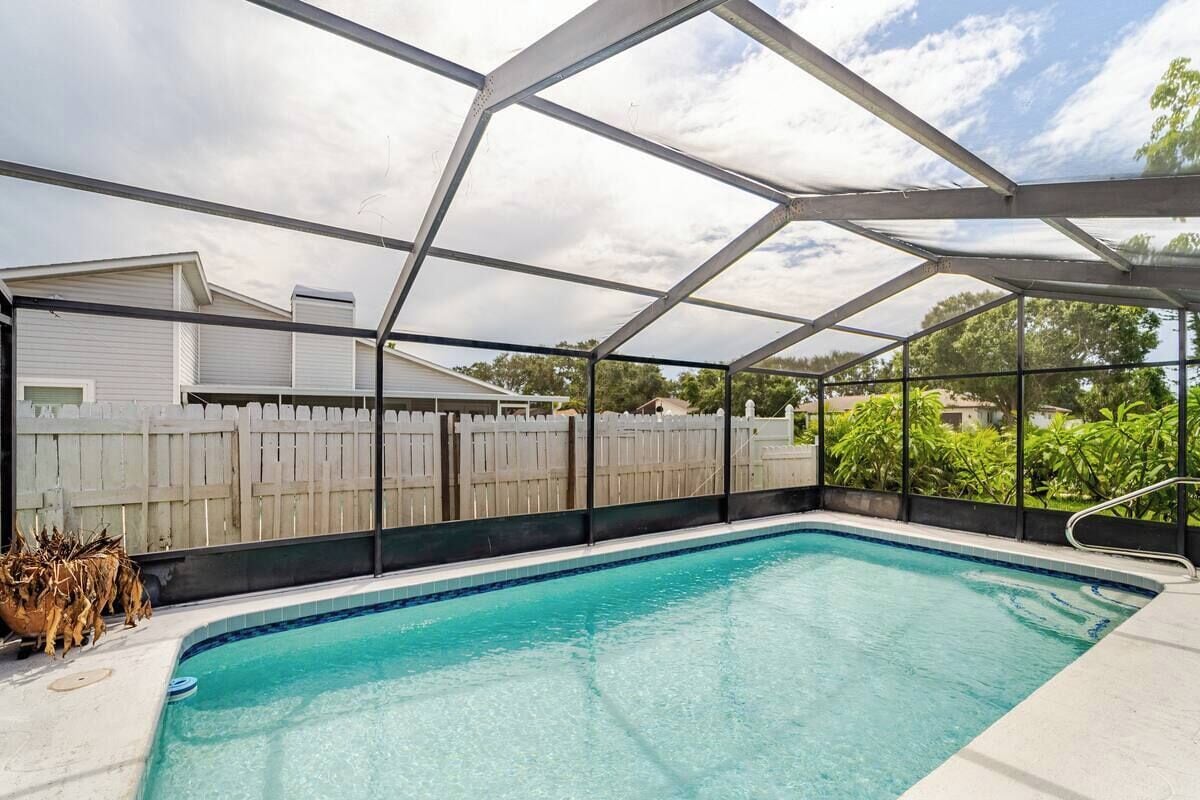 Una piscina con agua cristalina azul, rodeada por una valla blanca y una estructura de techo metálico.