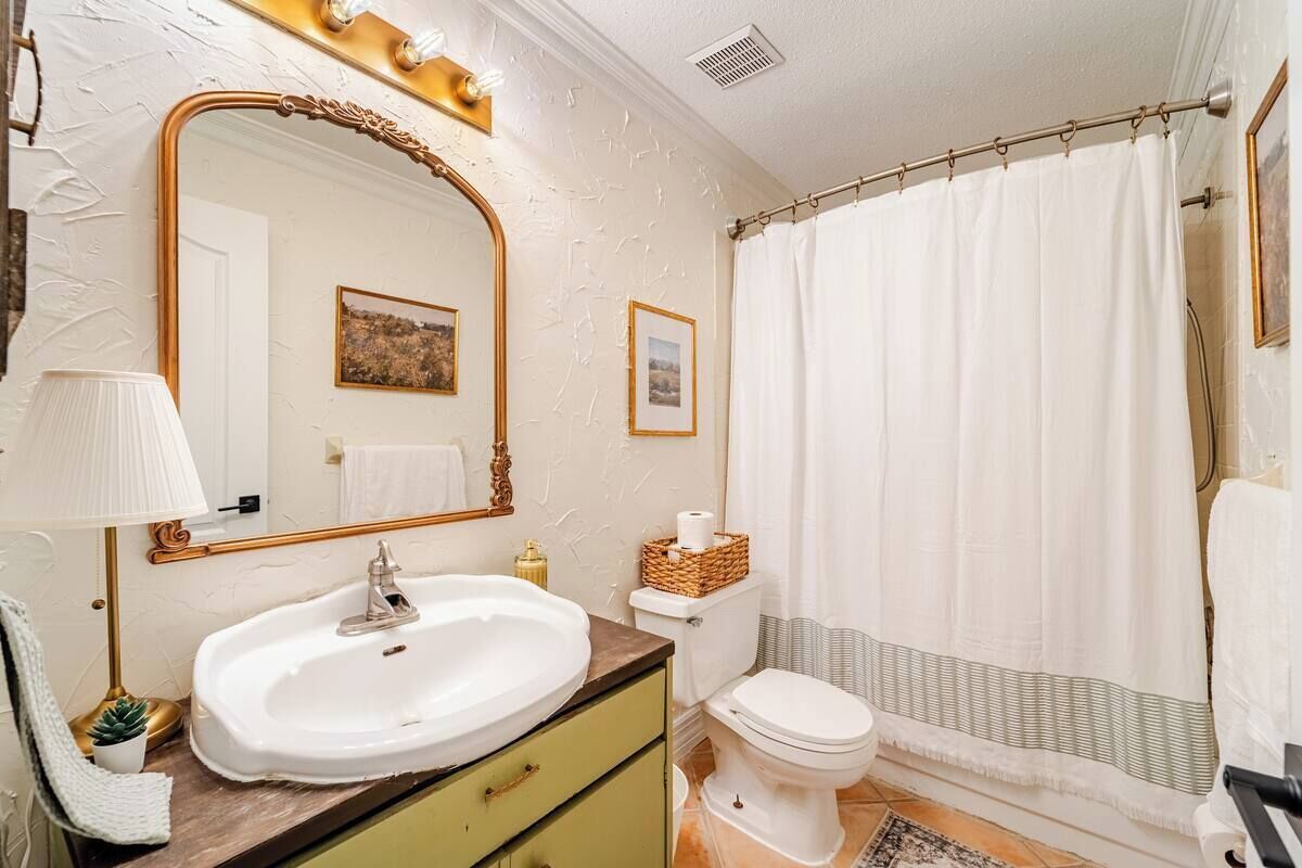 A bathroom with a white sink, a gold-framed mirror, a toilet, and a shower curtain.