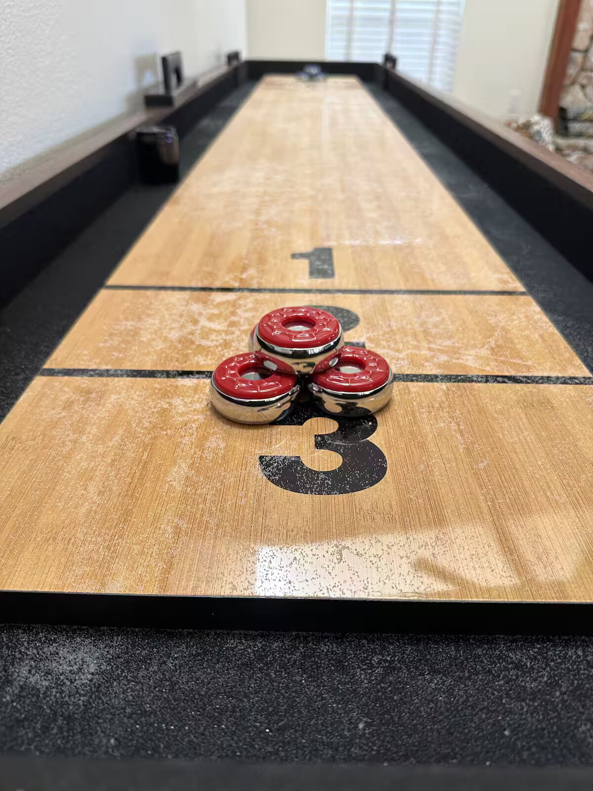 A shuffleboard table with three red pucks stacked on the 3 spot.