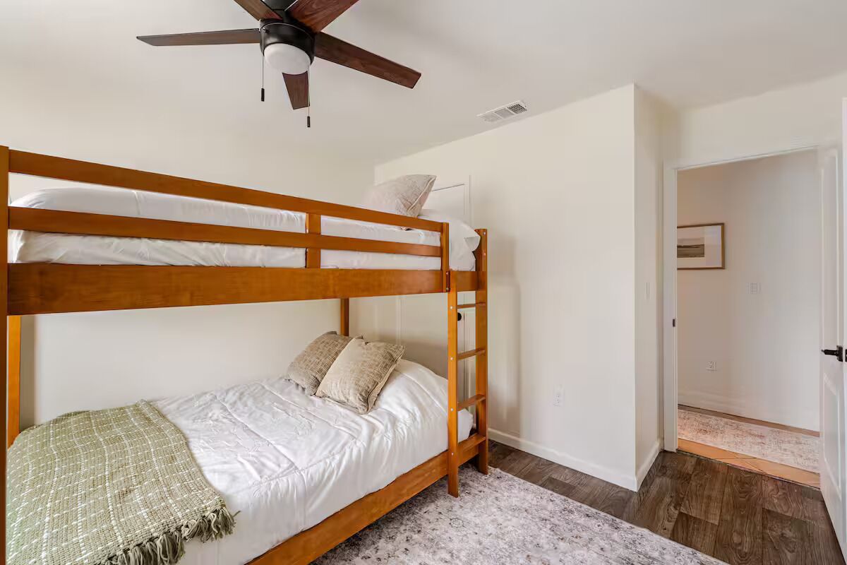 Un lit superposé avec une échelle, du linge de lit blanc et un ventilateur de plafond.