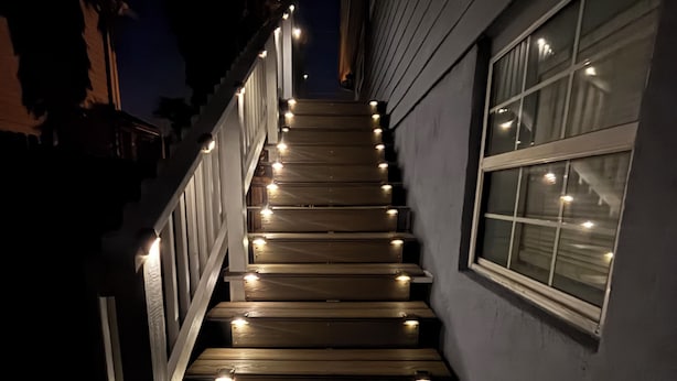 A wooden staircase with lights along the steps, leading up to a window.