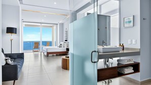 A modern hotel room with a balcony, a bed, a bathroom with a large mirror, and a view of the sea. - Beachfront 2BR - Pools & Balcony Views (Puerto Vallarta)