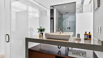 A modern bathroom with a large mirror, a white sink, and a wooden vanity.