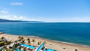 A beach resort with a pool area, palm trees, and a view of the ocean. - Beachfront 2BR - Pools & Balcony Views (Puerto Vallarta)