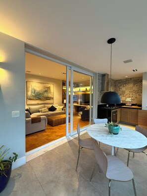 A modern interior with a dining area, a sofa set, and a kitchen visible through a glass door.